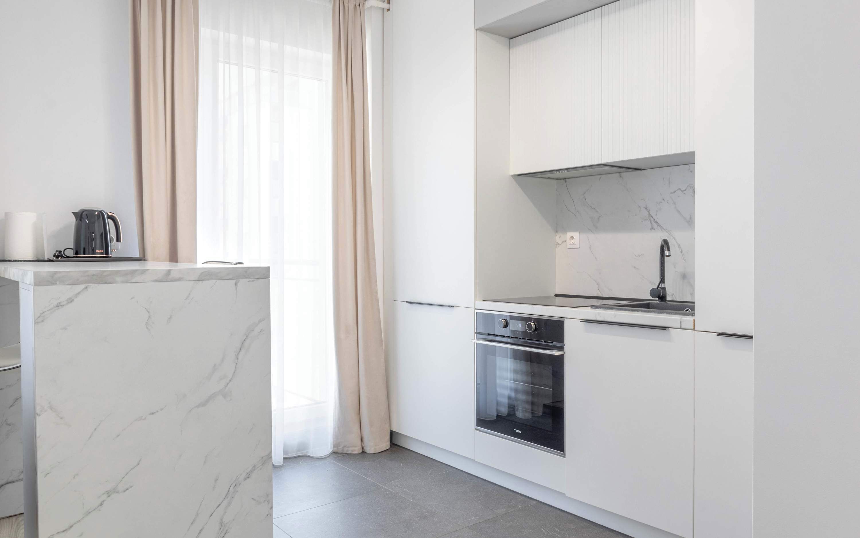 Een moderne keuken met witte kastjes, een inbouwoven en een roestvrijstalen spoelbak.