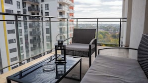 Un balcon doté d'une balustrade en verre, d'une chaise en osier, d'un banc rembourré, d'une table en verre et d'un porte-bougie.