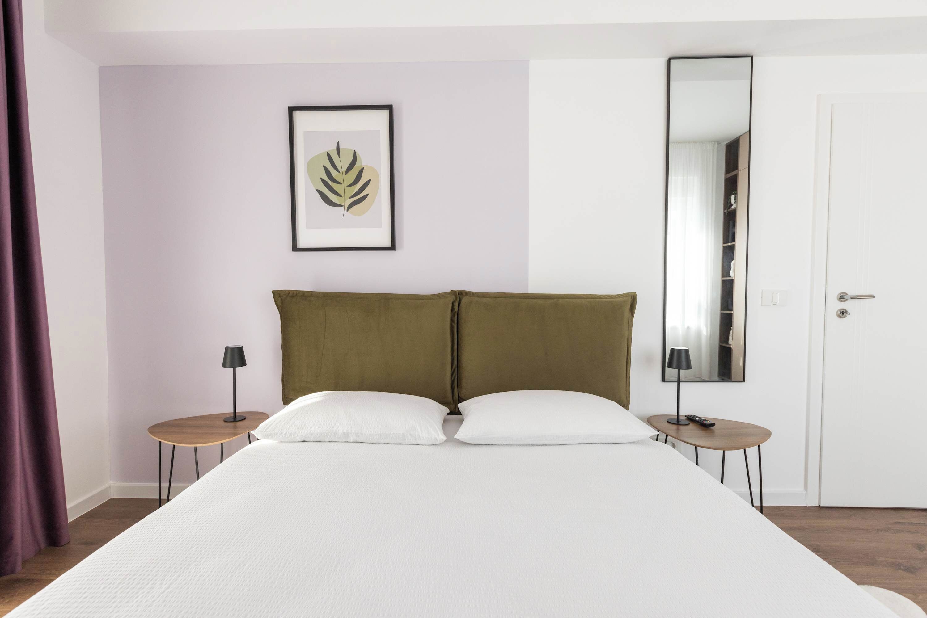 Een slaapkamer met een bed, twee nachtkastjes, een kunstwerk van een blad in een lijst, een spiegel en een kledingkast.