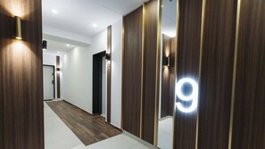 Un couloir moderne avec un lambris en bois, un panneau lumineux portant le chiffre 9 et un sol carrelé.