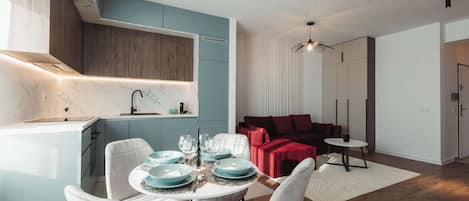 A modern kitchen with marble countertops, a dining area with white chairs and blue plates, and a red sofa in a living area.
