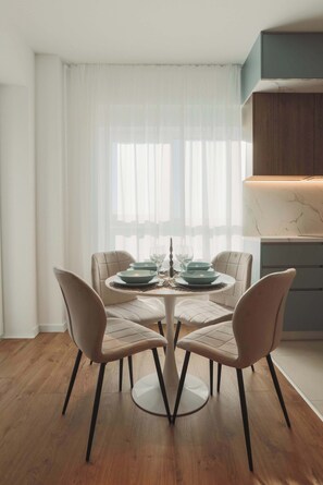 Un coin repas avec une table ronde, quatre chaises et une fenêtre ornée de rideaux légers.