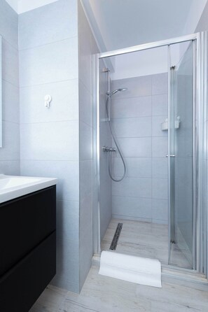 A modern bathroom with a glass shower enclosure, a white sink, and a black cabinet.