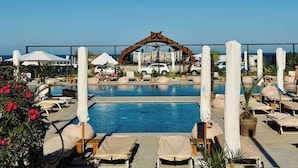 Uma área de piscina com espreguiçadeiras, guarda-sóis e um arco decorativo.