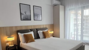 Quarto de hotel moderno com uma cama grande, duas mesas de cabeceira com luminárias, um ar condicionado fixado na parede e duas imagens emolduradas.