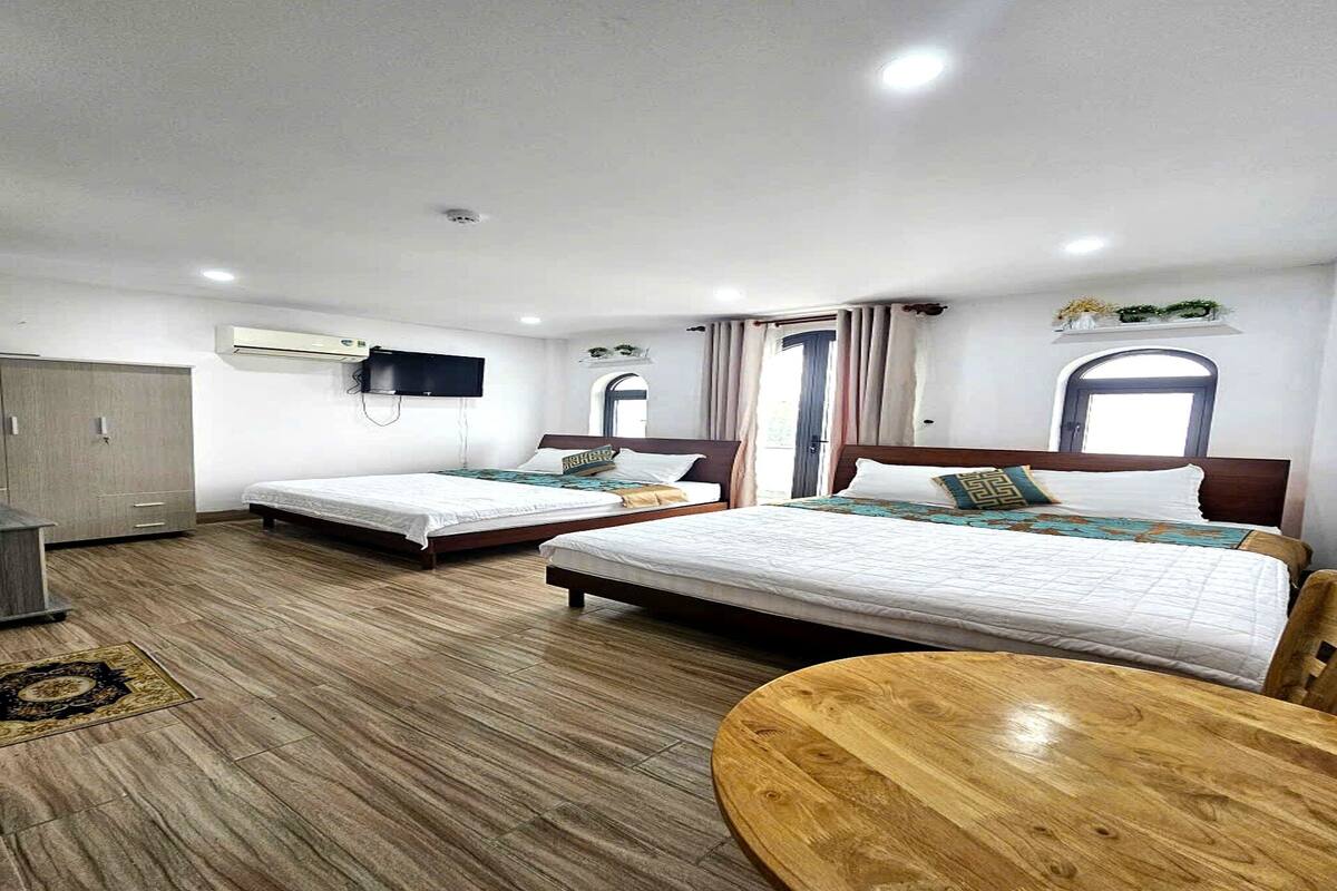 A hotel room with two beds, a wooden floor, a TV, and a window.
