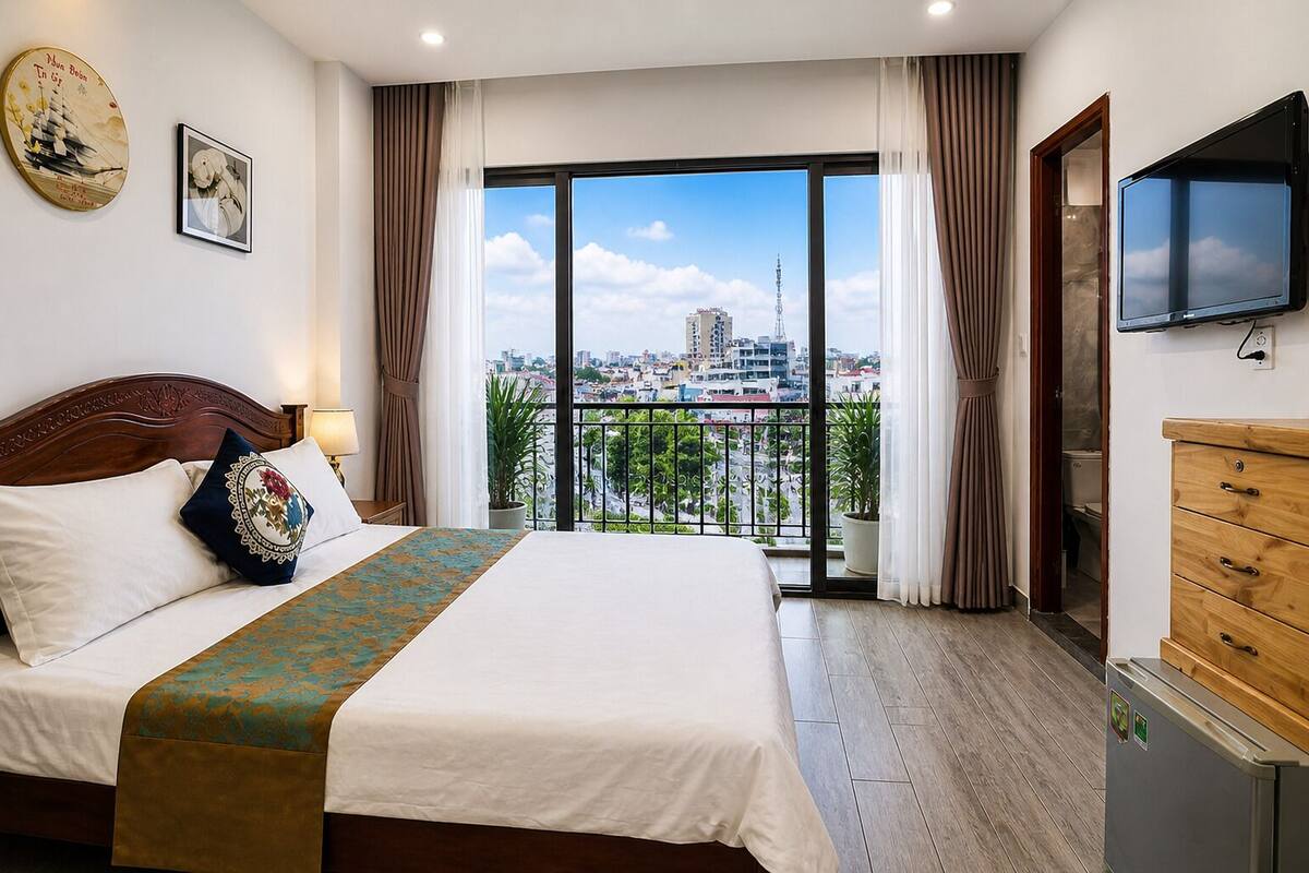 A hotel room with a large bed, a TV, a wooden dresser, and a balcony with a city view.