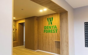 Un couloir aux murs lambrés, sur lequel est accrochée une pancarte indiquant « FORÊT DE DENYA ».