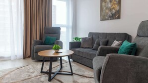 A modern living room with a grey sofa, a matching armchair, a small round table, and a potted plant.