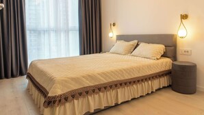 A neatly made bed with a quilted cover, two pillows, and a decorative border. There are two wall-mounted lights on either side of the bed.
