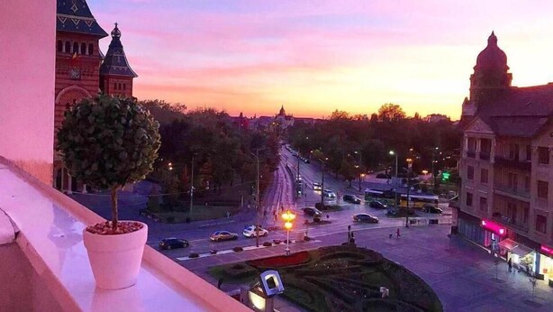 Un paisaje urbano al atardecer con edificios históricos, una fuente y un árbol en una maceta.