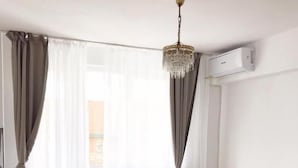 Un dormitorio moderno con una cama de madera, ropa de cama blanca, una araña y un equipo de aire acondicionado.