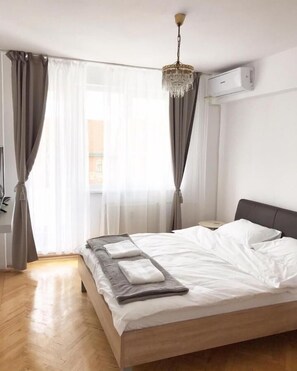 Ein modernes Schlafzimmer mit einem hölzernen Bett, weißen Leinen, einem Kronleuchter und einer Klimaanlage.