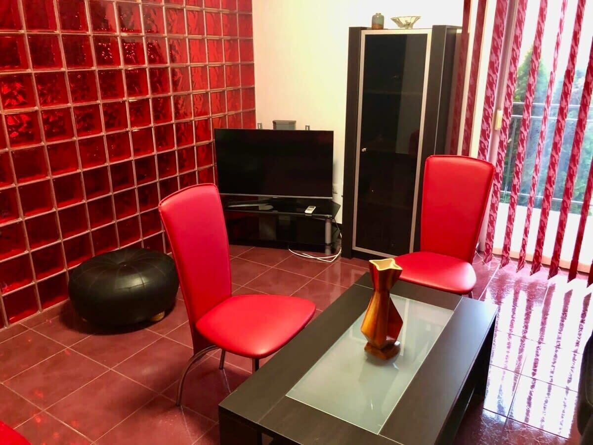 A modern living room with red chairs, a black sofa, a glass coffee table, and a TV.