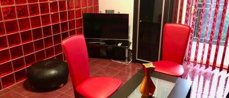 A modern living room with red chairs, a black sofa, a glass coffee table, and a TV.