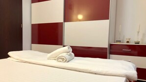 A neatly made bed with white linens and two rolled towels, a red and white dresser, and a mirror on the wall. - Joy City Stay Calea Timisoarei 4 (Timișoara)