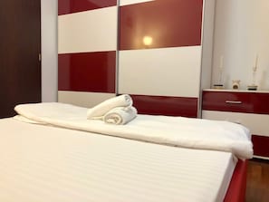 A neatly made bed with white linens and two rolled towels, a red and white dresser, and a mirror on the wall. - Joy City Stay Calea Timisoarei 4 (Timișoara)
