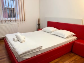 Ein Bett mit weißer Bettwäsche, einem roten Kopfteil und einem Nachttisch mit einer Vase.