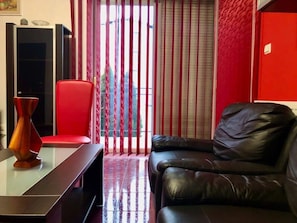 Ein Wohnzimmer mit einer schwarzen Ledersofa, einem roten Sessel, einem Glastisch und einem TV-Schrank.