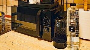 Een keuken met een magnetron, waterkoker en een waterfles op het aanrecht.