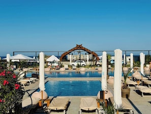 Un espace piscine agrémenté de chaises longues, de parasols et d’une arche décorative.