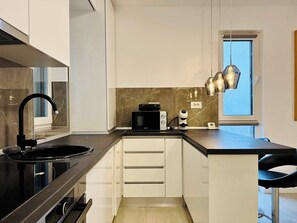 Eine moderne Küche mit schwarzem Arbeitsplatz, weißen Schränken, einem eingebauten Backofen und einem Fenster mit Ausblick.