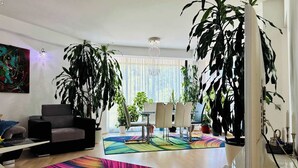 A modern living room with a sofa, a dining table with chairs, large potted plants, and colorful rugs. - Joy City Stay - Memorandului (Timișoara)