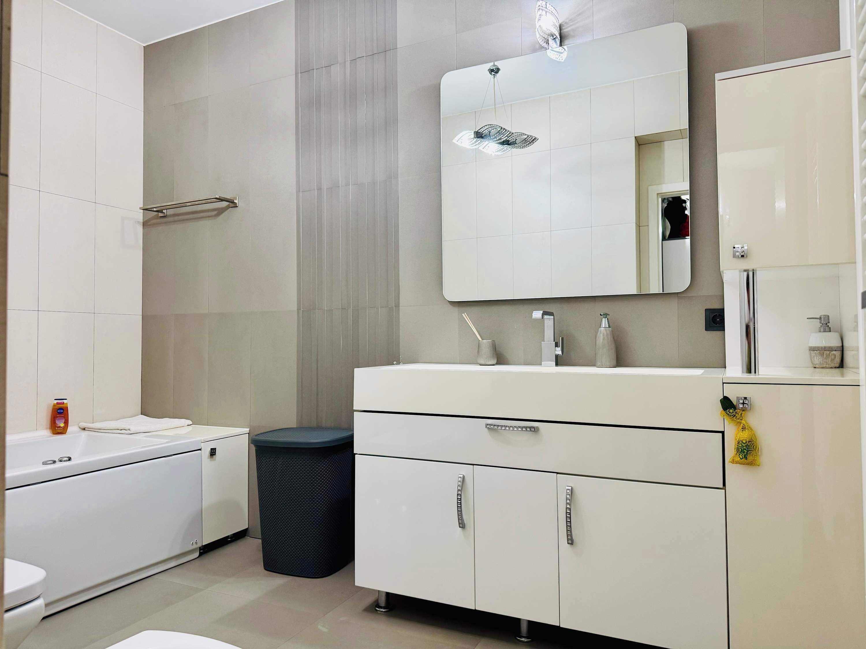 Une salle de bain moderne avec un meuble-lavabo blanc, un miroir, des toilettes et une poubelle.