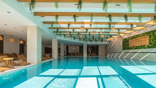 A swimming pool with wooden beams and hanging plants, lounge chairs, and a wall with a sign. - Joy City Stay - Memorandului (Timișoara)