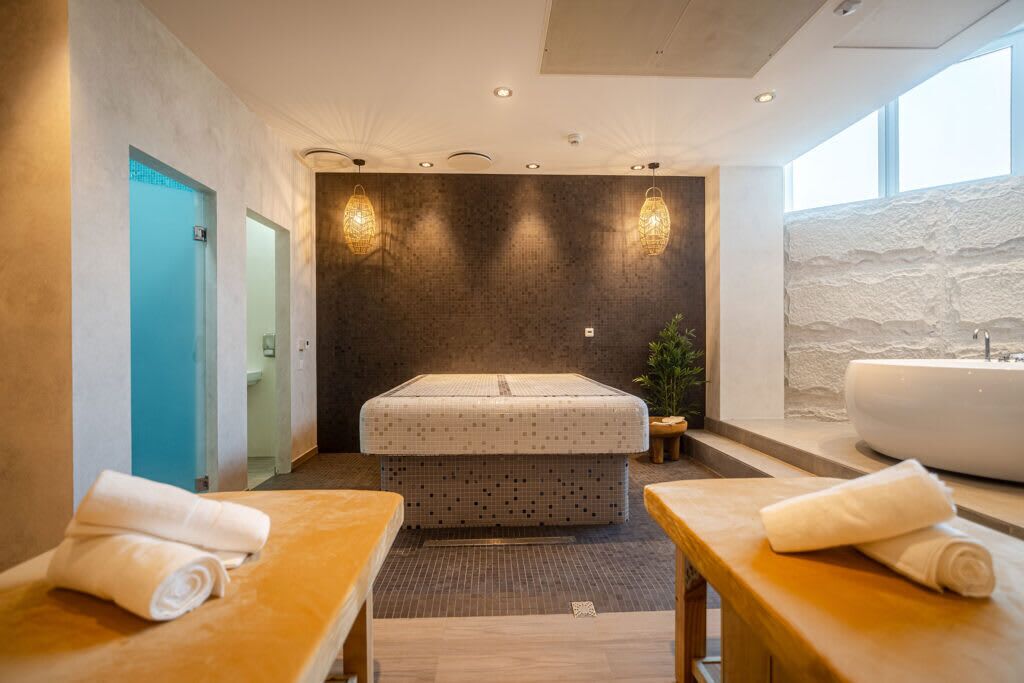 A modern bathroom with a large bathtub, a separate shower area, and two wooden tables with towels.