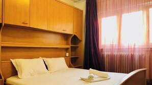 A neatly made bed with white linens and a rolled towel, wooden headboard, and built-in wooden shelves. - Joy City Stay Family Ultracentral (Timișoara)