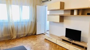 A modern living room with a flat-screen TV, wooden flooring, and a sliding door. - Joy City Stay Family Ultracentral (Timișoara)