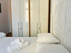 A neatly made bed with white linens and towels, a white metal headboard, and a wardrobe with vertical wooden accents. - Joy City Stay  Unirii 1 (Timișoara)