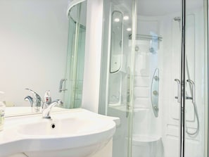 A modern bathroom with a white sink, two faucets, a glass shower enclosure, and a mirror. - Joy City Stay  Unirii 1 (Timișoara)