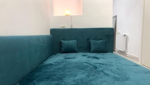Habitació petita amb un llit individual, un edredó color aquamarina, una làmpada penjada a la paret i una finestra amb vista a l'exterior.