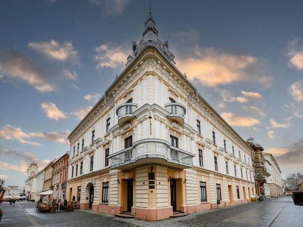 Ein historisches Gebäude mit aufwendiger Architektur, einem Hauseingang an der Ecke und einer gepflasterten Straße.