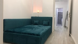 Un dormitori amb un llit verd maragda, una làmpada de nit i vista a un passadís.