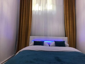 Ein Bett mit blauer Bettdecke, weißen Kissen und einem Kopfteil mit blauer Beleuchtung.
