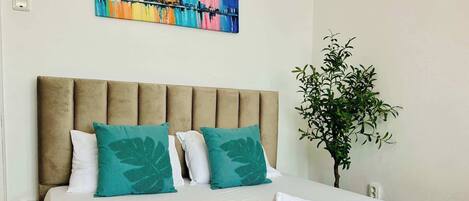 Una habitación de hotel con una cama, cabecera, un cuadro y una planta en maceta.