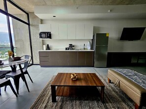 A modern kitchen with white cabinets, a dining area with a table and chairs, and a living area with a sofa and a coffee table. - Studio Apartment in San Benito, with balcony & volcano views. (San Salvador)