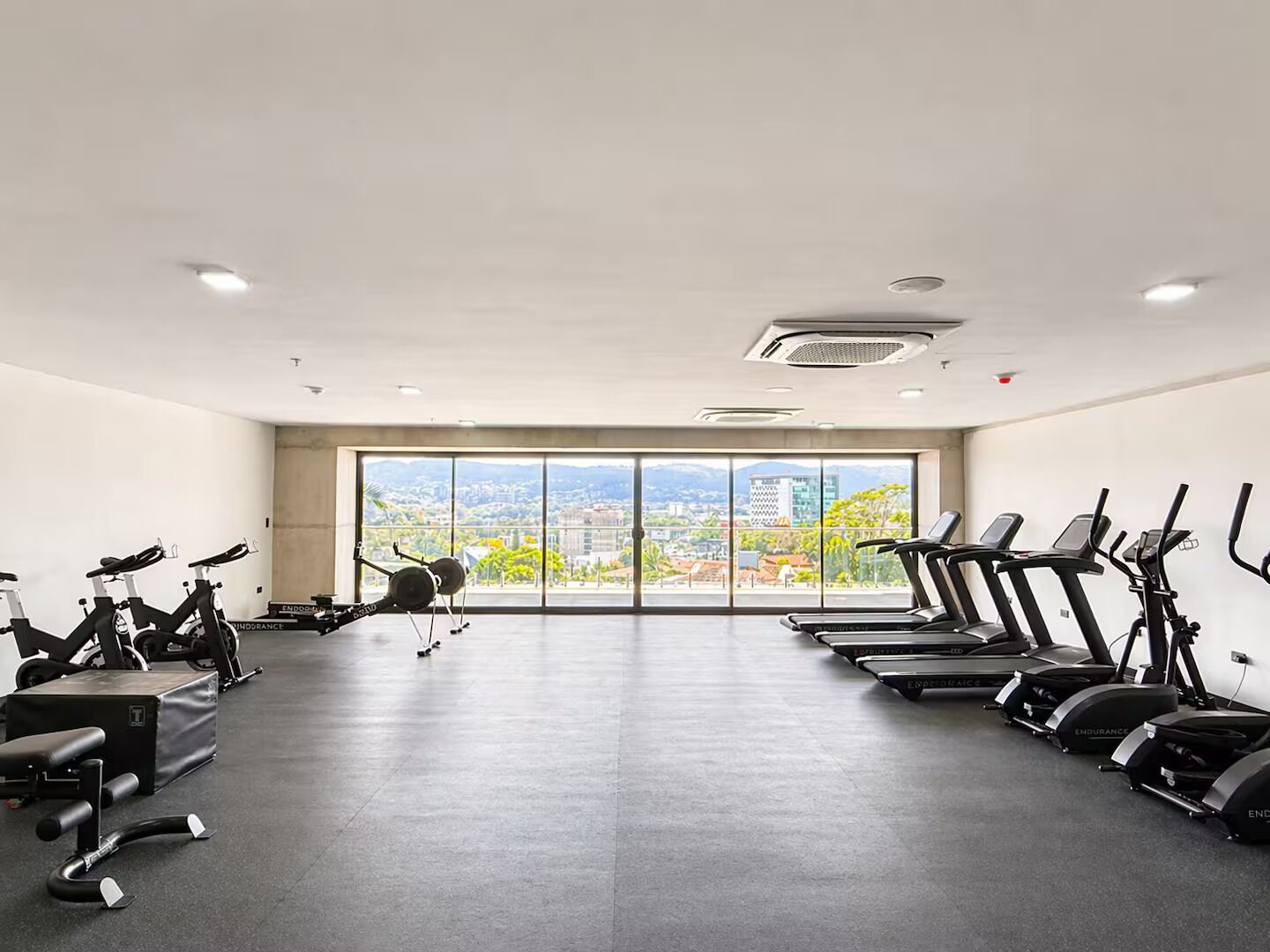 Ein Fitnessstudio mit Ergometer, Laufbändern und Krafttrainingsgeräten, große Fenster mit Blick auf die Stadt.