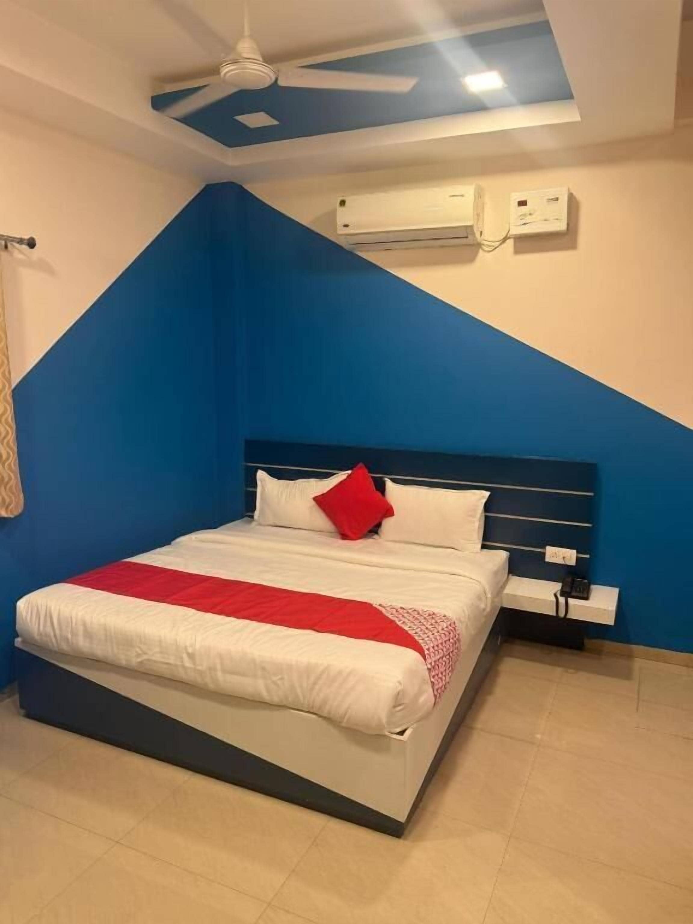 Un dormitorio con una cama, un almohadón rojo, una mesita de noche blanca y un equipo de aire acondicionado.