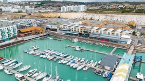 A marina with numerous boats docked, a commercial area with buildings, and a hilly landscape in the background. - Cozy 1BR Seaside Apt in Brighton Marina Village (Brighton and Hove)