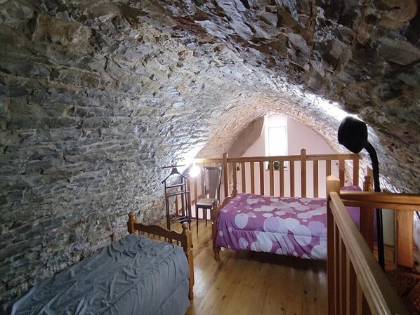 A bedroom with a sloped ceiling, a wooden bed, a chair, and a desk. - "2** Vacation Rentals in La Couvertoirade: 'LE LARZAC'" (La Couvertoirade)