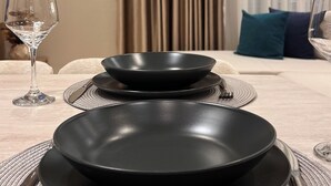 Een eettafel gedekt met zwarte borden, bestek en een wijnglas, met een gordijn en een airconditioner op de achtergrond.