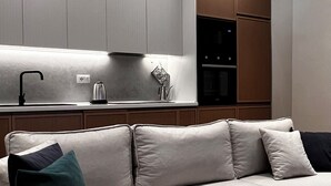 Een moderne woonkamer met een bank, een salontafel en een keuken met kasten en apparatuur.