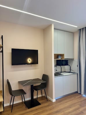 Una cocina moderna con microondas integrado, una zona de comedor con mesa y sillas, y un televisor de pantalla plana montado en la pared.