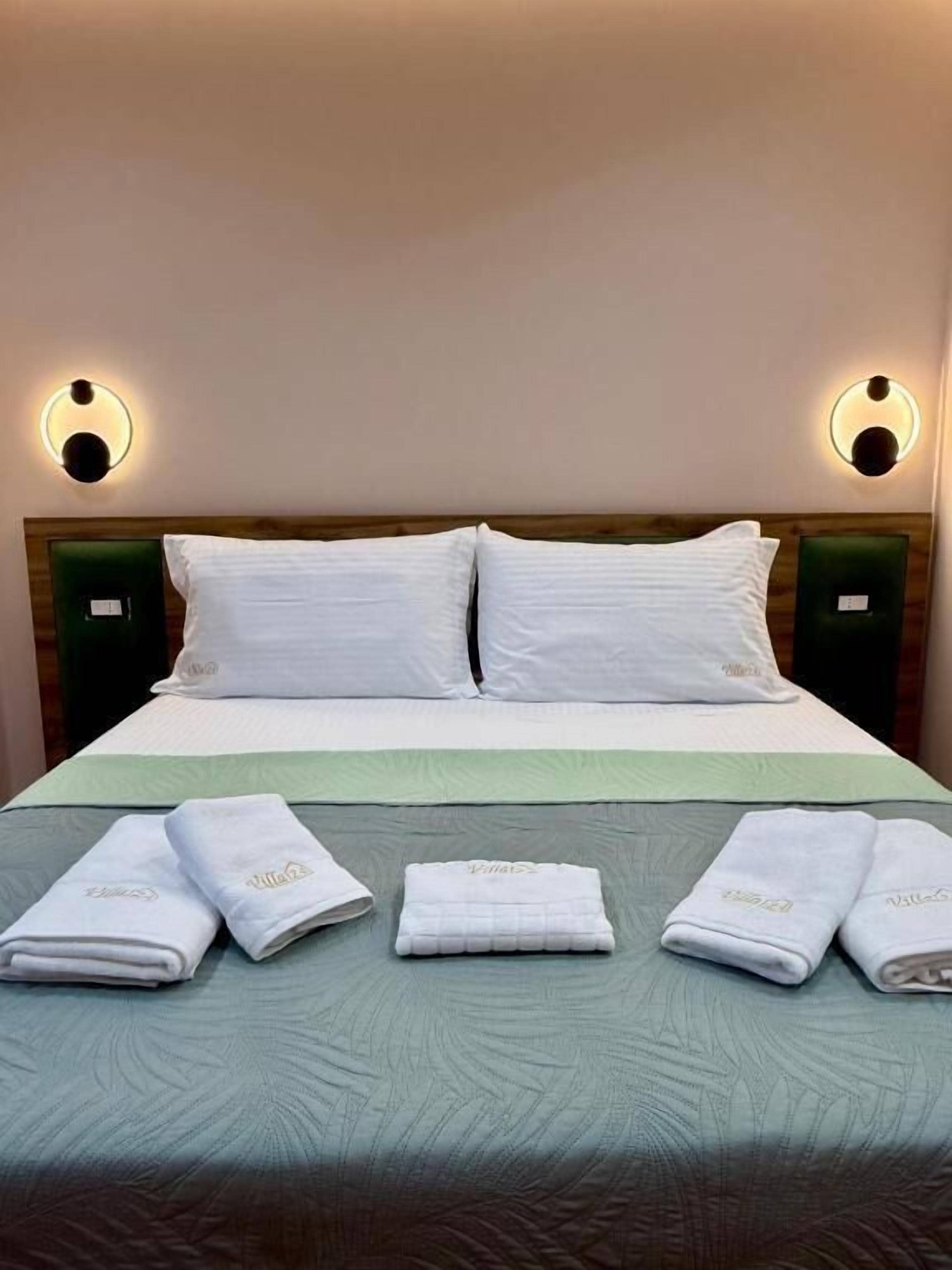 A hotel room with a bed, two pillows, two bedside tables with lamps, and four towels on the bed.