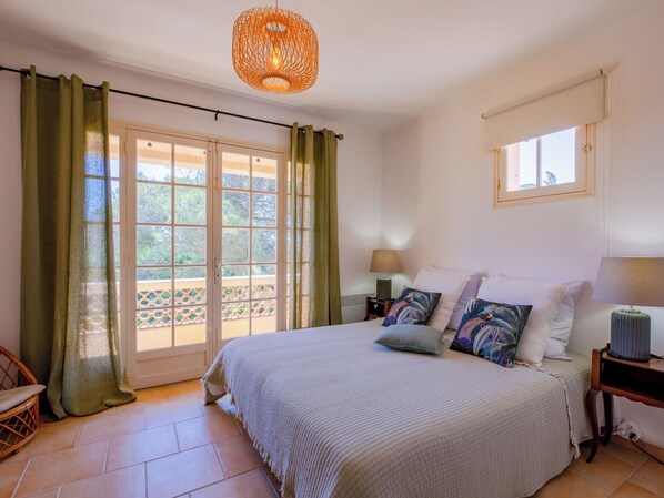 Un dormitorio con cama, cortinas, mesita de noche, lámpara, ventana y vistas al exterior.