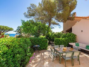Eine Terrasse mit Esstisch, umgeben von üppiger Vegetation und Blick auf das Meer.